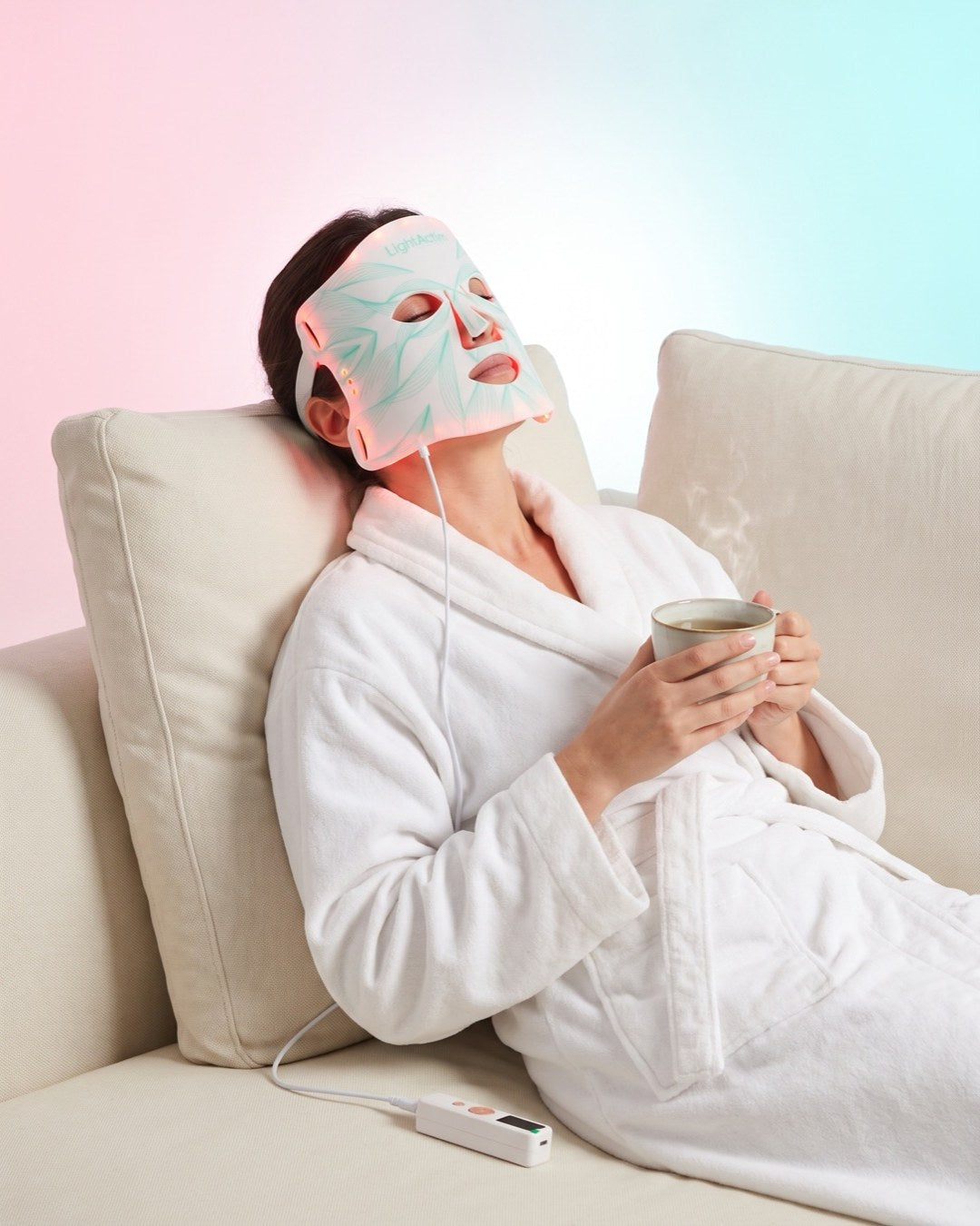 Femme se détendant avec le masque LED visage Bodysiam, une tasse de thé à la main