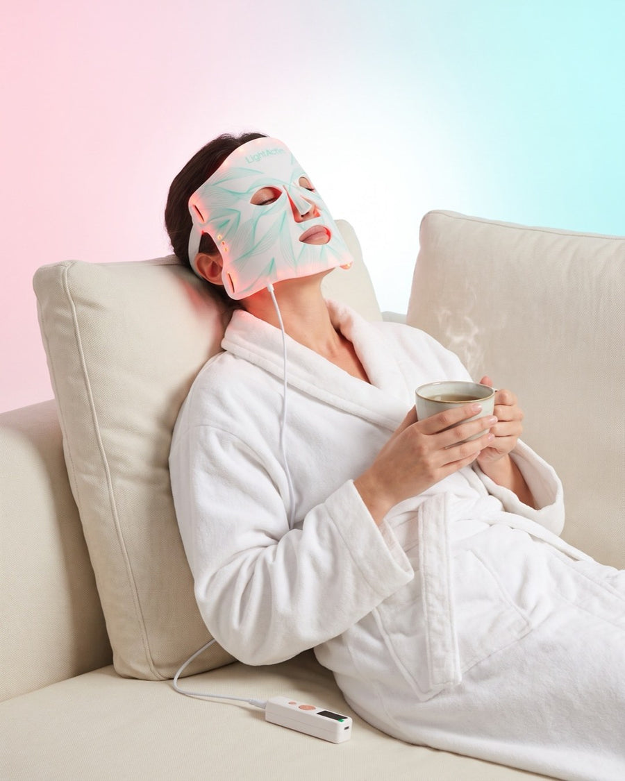 Femme se détendant avec le masque LED visage Bodysiam, une tasse de thé à la main